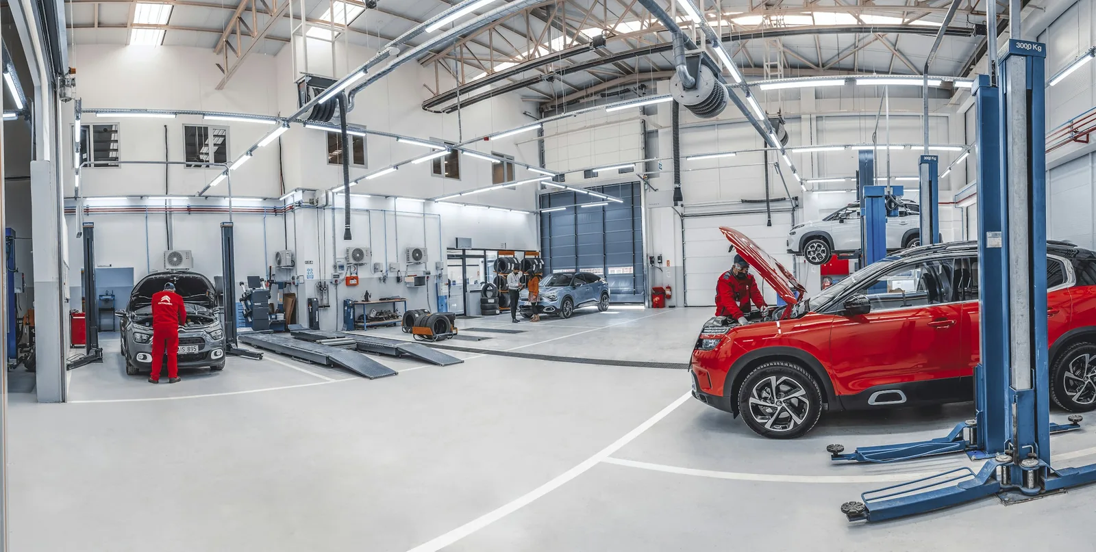 Světlá servisní hala s auty na zvedácích a mechaniky při práci
